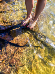 Young woman standing on rocks in water. Bare feet and legs with pink nailpolish. Karlstad, Värmland, Sweden.