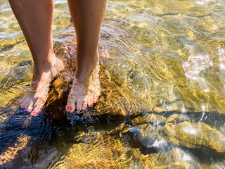 Young girls feet standing on rocks in water. Waves and sunshine. Karlstad, Värmland, Sweden.