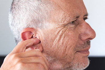 Senior man with unshaved stubble beard picking his ear with index finger. Close up image.