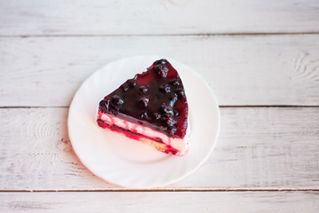 Piece of cheesecake with black currant and blueberry sauce on white plate on wooden table. Unique delicious dessert.