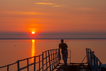 Morning fishing. Fisherman on the background of the sunrise.