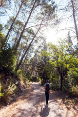 Fototapeta na wymiar Young adventurer on his back with backpack walking while traveling on offroad nature tourism in the middle of the forest in the Cazorla Natural Park, in Spain. Selective focus.