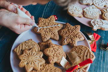 Boy is decorating gingerbread cookies with icing sugar. Snowflake, star shapes.	
