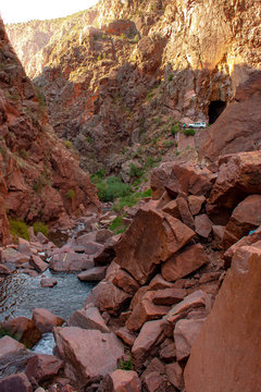 Mountain stream flows through red rock desert canyon with road and tunnels in background, located in Gilman Tunnels, Jemez Mountains, New Mexico, USA
