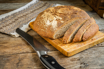 Sliced homemade bread with a kitchen napkin and a knife on a wooden table. Village life. Home cooking.