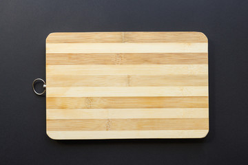 a wooden chopping board with a striped surface in dark and light wood and a ring on a dark background.