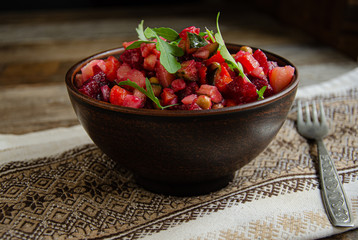 Vegetable salad, vinaigrette, in a ceramic earthenware, a folkloric bowl with a kitchen napkin on a wooden table. Village life. Home cooking.