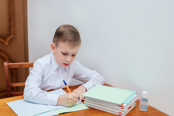 the boy is sitting at the table, holding a pen, next to notebooks and textbooks
