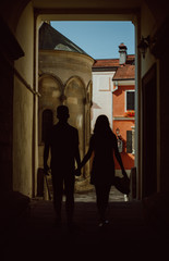 Silhouette of young couple walking the arch and holding each other hands. Girl holding hat in the hand.