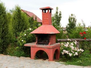 Barbecue in summer garden among trees and beautiful blooming red, pink and white roses.