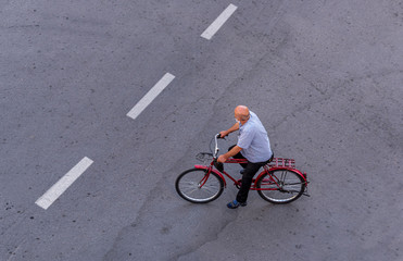 Top view of an elderly bald man wearing a surgical mask on the street and riding a bicycle