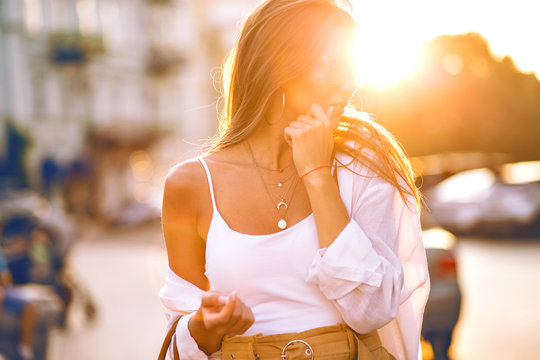 Sensual summer sunny portrait of elegant hipster blogger woman wearing minimalistic casual outfit, clear glasses and gold accessories, powerful sunlight.