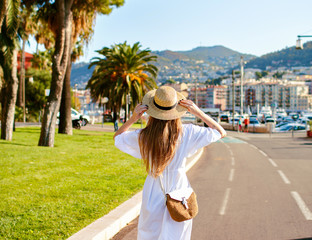 Young woman posing nice beautiful France Riviera city, wearing trendy elegant feminine dress and straw accessories, posing back end enjoying the view, traveling goals.