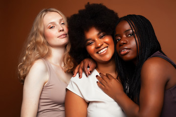 young pretty caucasian, afro, scandinavian woman posing cheerful together on brown background, lifestyle diverse nationality people concept