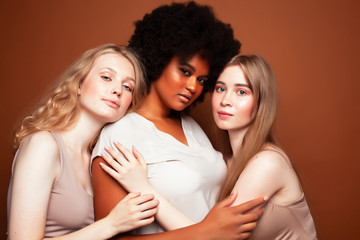 Obraz premium young pretty caucasian, afro, scandinavian woman posing cheerful together on brown background, lifestyle diverse nationality people concept