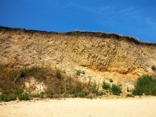 Deep sandy cliff on the background of blue sky. The destruction of the coast as a consequence of soil erosion. Landslide - threat to life.