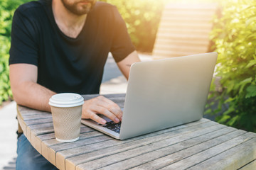 Cropped shot of casually dressed bearded freelancer man sitting outdoors working on his laptop