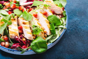 Salad with grilled chicken, spinach, arugula, cedar nuts and pomegranate seeds. Healthy food and eating concept. Top view. Blue background