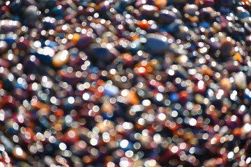 Blurred multicolored sea pebbles. Abstract example of a fragment of the shore with sun glare