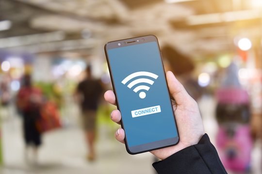 Close-up Of Hand Holding Mobile Smartphone With Wifi Connect On Blurry Shopping Mall Background.