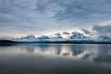 Fototapeta na wymiar A cloudy day at Jackson Lake in Wyoming, USA at the Grand Teton National Park. Low lying clouds are surrounding the mountains and reflecting onto the lake. 