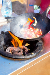 Tossing vegetables in a wok. Cook prepares a dish with fresh vegetables outdoors.