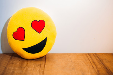 Emoji enamorado, sonriendo e iluminado posado sobre una mesa de madera