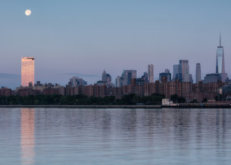 View on Downtown Manhattan from East river at sunrise with full moon set .