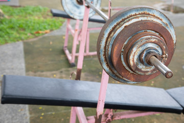 Selective focus and perspective view of old, grunge and rusty barbell equipment in the public outdoor gym which is free of charge for everyone in the community nearby is available for healthy life