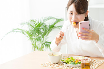 Obraz na płótnie Canvas 食事をしながらスマホを見る女性