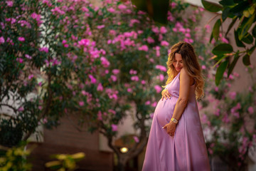 Fototapeta premium beautiful young pregnant girl in a purple dress stands on the stairs against the background of a flowering tree