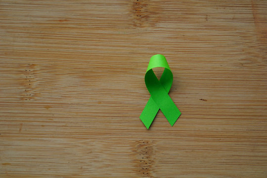 green ribbon as symbol of fighting cancer illness on wooden board with copy spacered ribbon as symbol of fighting cancer illness on wooden board with copy space