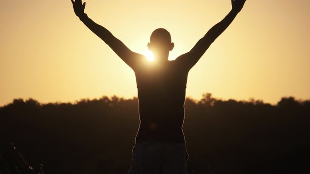 Silhouette of Young Man against Sunset Raising Hands Sides and Up. Slow Motion