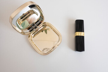 gold mirror and lipstick in a black case on a white table..