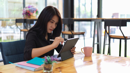 Portrait of female freelancer focusing with digital tablet on worktable