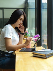 Side view of female freelancer using digital tablet with keyboard and stylus in coffee shop