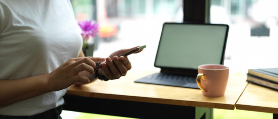 Female using smartphone while sitting at worktable with mock up tablet