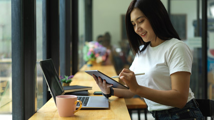 Female college student doing assignment with digital tablet and laptop in cafe