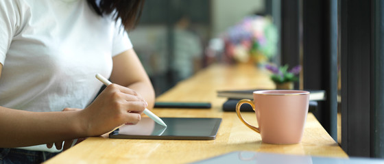 Fototapeta na wymiar Side view of female hand using digital tablet on wooden bar in cafe