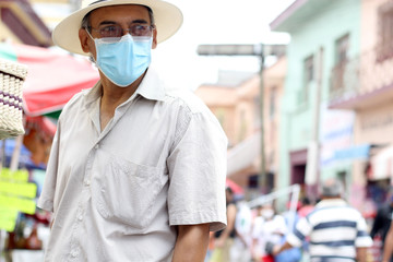 Latino older adult with protective face masks and hat walking in plaza, new normal covid-19