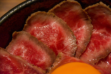 霜降り牛肉のスライスで埋め尽くされたローストビーフ丼、卵黄トッピング。一人前。外食、昼ご飯、食堂、オープンキッチン。口コミ、グルメ、行列、人気店。丼物。丼鉢。肉屋。肉々しい。刺身。造り。ユッケ。生物。ナマモノ。レア。黄身。