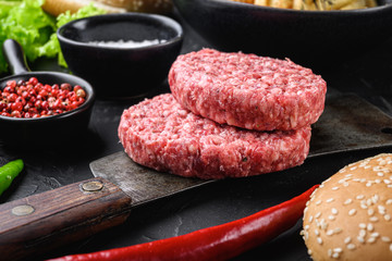 Raw ground beef cutlets with ingredients for burger on black background
