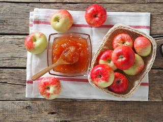 Apple jam surrounded by apples on a napkin on a wooden background. Autumn still life with apples.