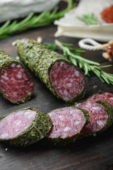 Variety of dry cured  chorizo, fuet and other sausages cut in slices with herbs on dark wooden background