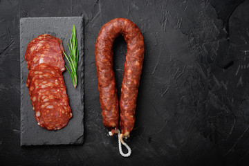 Whole and sliced chorizo sausage on black background, flat lay with copy space