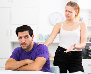 Obraz premium Frustrated guy sitting at home table on background with dissatisfied girlfriend