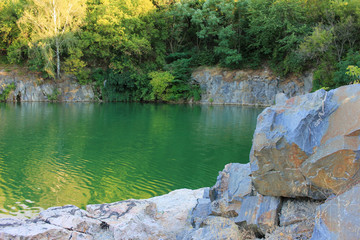 Mountain lake in the summer. Panoramic view on old flooded granite quarry with radon water. Landscape with rock stones, green trees and clean pond