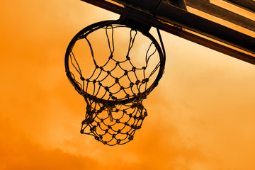 A basketball hoop with net at an outdoor basketball court seen from the back, silhouette against...