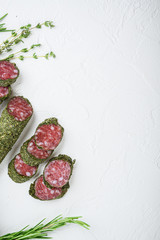 Traditianal fuet sausage in herbs with ingredients on white surface, flat lay with copy space