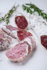 Dry cured fuet salami sausage slices with herbs on white surface